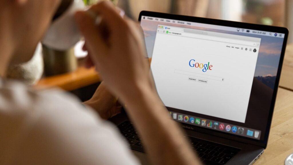 Bir kişi, laptop ekranında açık olan Google ana sayfasına bakarken kahve içiyor.