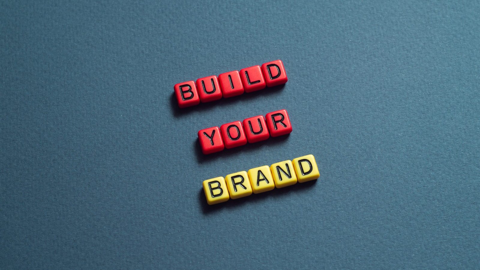 Kırmızı ve sarı harf küplerinden oluşan 'Build Your Brand' yazısı, marka oluşturmanın önemini vurguluyor.